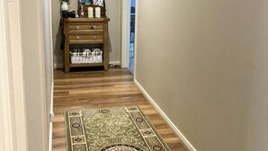Un couloir avec un tapis à motifs, un plancher en bois, une commode contenant divers objets et des tableaux encadrés accrochés aux murs.
