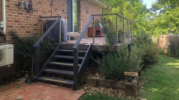 Une maison en briques dotée d’un espace extérieur couvert, d’un escalier menant à une terrasse et d’une pancarte de bienvenue.