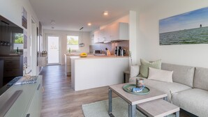 A modern kitchen with a central island, a dining area with a table and sofa, and a view of the sea. - Apartment "Ankergold" with Dike View, Balcony & Wi-Fi (Nordstrand)