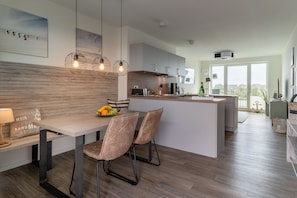 Een moderne keuken met een centraal eiland, hanglampen en een eethoek met stoelen.