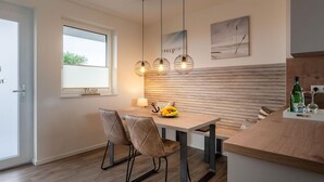 A modern kitchen with a wooden table, two chairs, pendant lights, and a view of the outdoors. - Apartment "Ankergold" with Dike View, Balcony & Wi-Fi (Nordstrand)