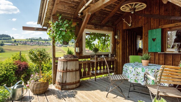 A wooden deck with a table and chairs, a hanging plant, and a view of a village. - Apartment "Oberberg" with Garden & Wi-Fi (Oberreute)