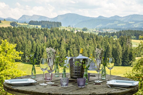 A table set outdoors with a scenic mountain view, a metal bucket, and various glassware.