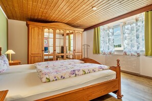 A bedroom with a wooden bed, a wooden wardrobe, a window with floral curtains, and a radiator.