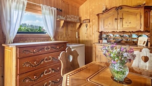 A wooden interior with a wooden dresser, a table with a vase of flowers, a clock on the wall, and a window with curtains. - Apartment "Oberberg" with Garden & Wi-Fi (Oberreute)