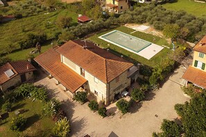Un bâtiment en pierre avec un toit recouvert de tuiles, une cour pavée et une piscine rectangulaire.