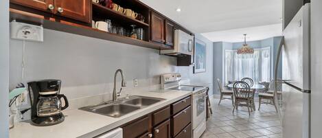A kitchen with a dishwasher, coffee maker, and a stove. There is a dining area with a table and chairs.