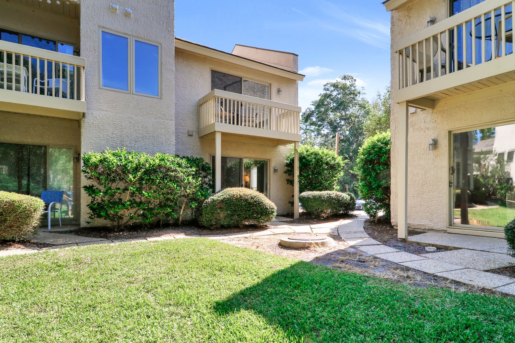 A residential building with a courtyard, featuring a covered patio, a small garden with manicured bushes, and a paved walkway.