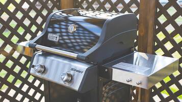 Una parrilla Weber Spirit con termómetro digital y perillas de control, sobre un fondo de celosía de madera.