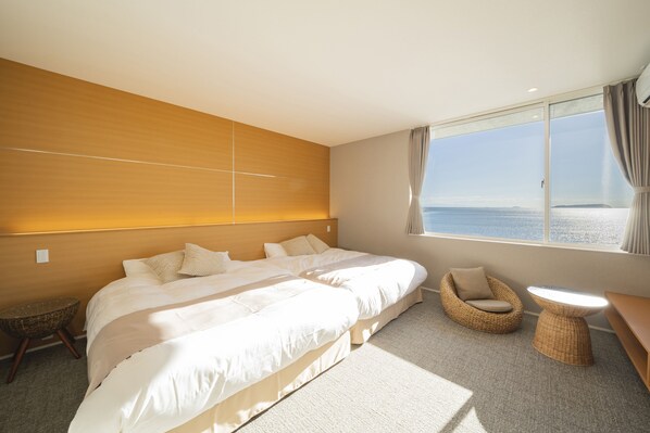 A hotel room with a large bed, a small sofa, a round table, and a view of the sea. - GLAMPREMIER Setouchi (Kanonji)
