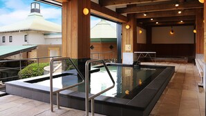 A spa area with a hot tub, wooden beams, and a view of a building with a green roof. - GLAMPREMIER Setouchi (Kanonji)