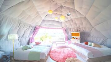 A tented accommodation with two beds, a desk, and a window with curtains.
