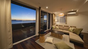 A modern living room with a large sliding glass door leading to a balcony, a sofa set, a coffee table, and a hanging light fixture. - GLAMPREMIER Setouchi (Kanonji)