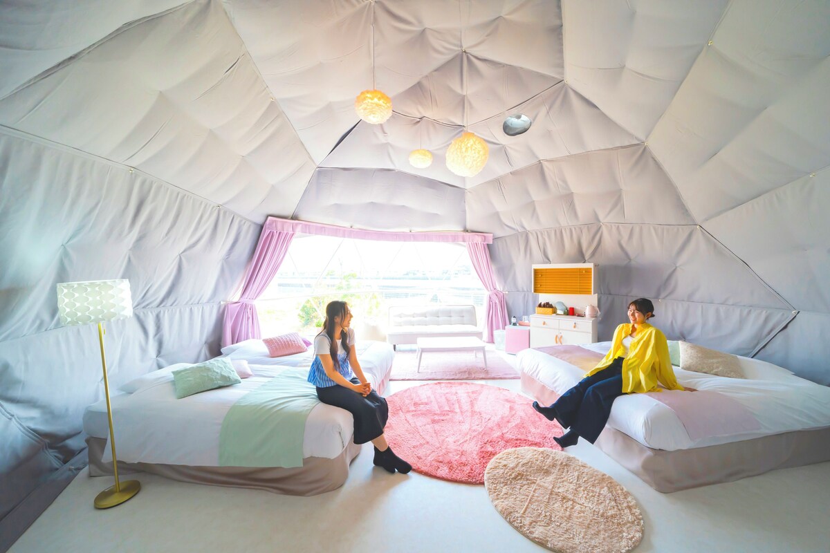 A tent-style room with two beds, a floor lamp, and a window with curtains.