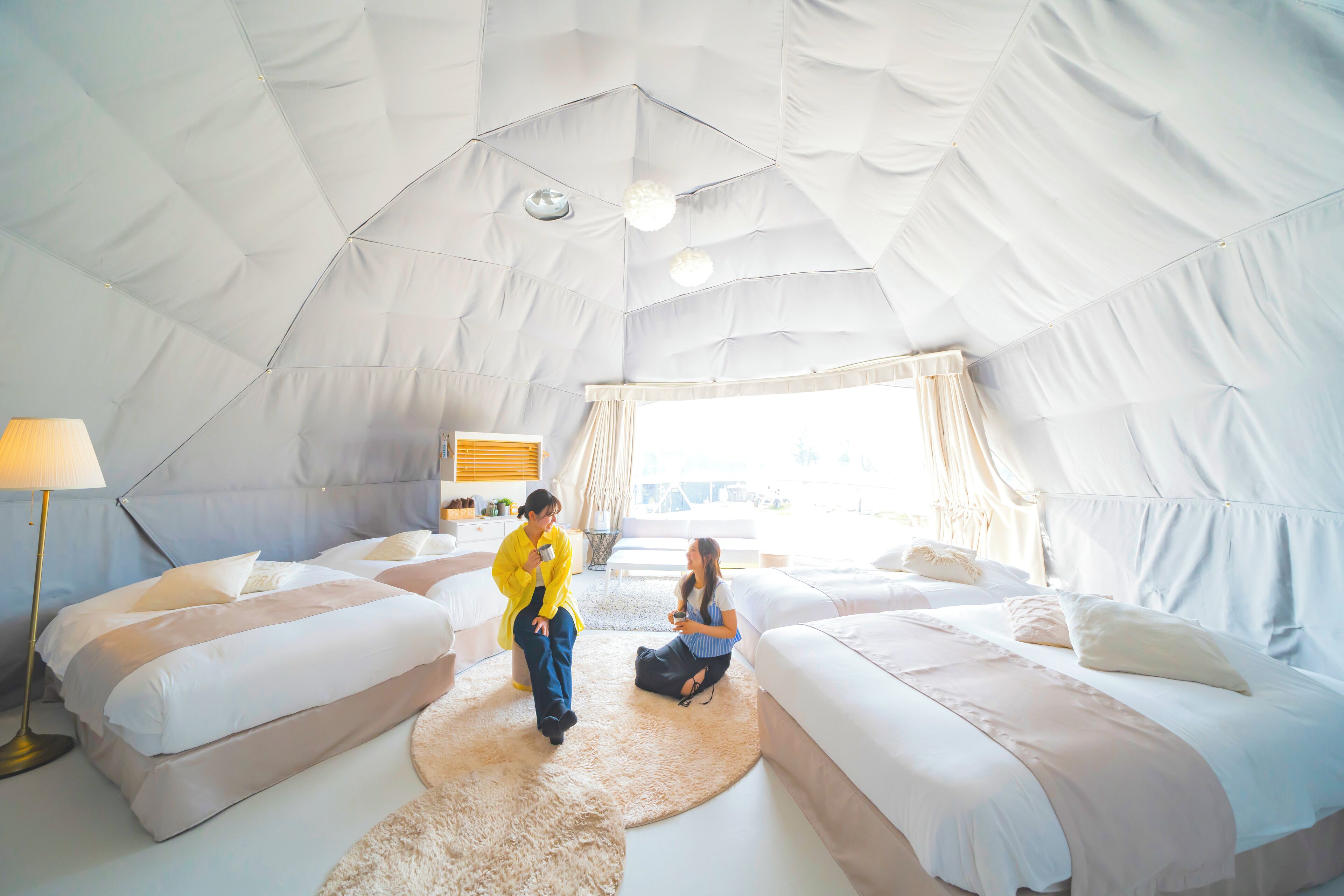 Um quarto amplo com tenda, duas camas, um tapete redondo e uma luminária.