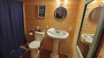 Un bagno con rivestimento in legno, un WC, due lavabi, uno specchio e una tenda da doccia.