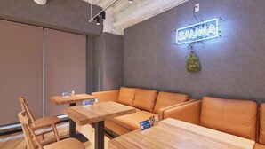 A modern interior with a neon sign reading "SAUNA" and a hanging plant. There are wooden tables and cushioned seating areas. - Rembrandt Cabin and Spa Shimbashi - Caters to Men (Tokyo)