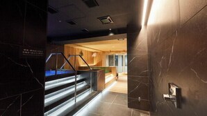 A modern hotel lobby with marble walls, a staircase with illuminated steps, and a reception area with wooden accents. - Rembrandt Cabin and Spa Shimbashi - Caters to Men (Tokyo)