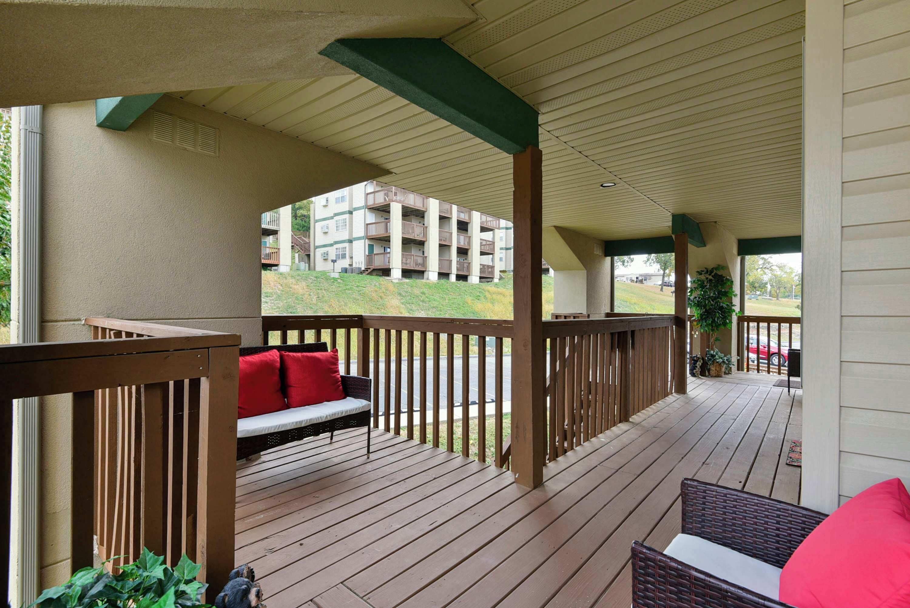 A covered outdoor deck with wooden railings, a bench with red cushions, and a wicker chair.