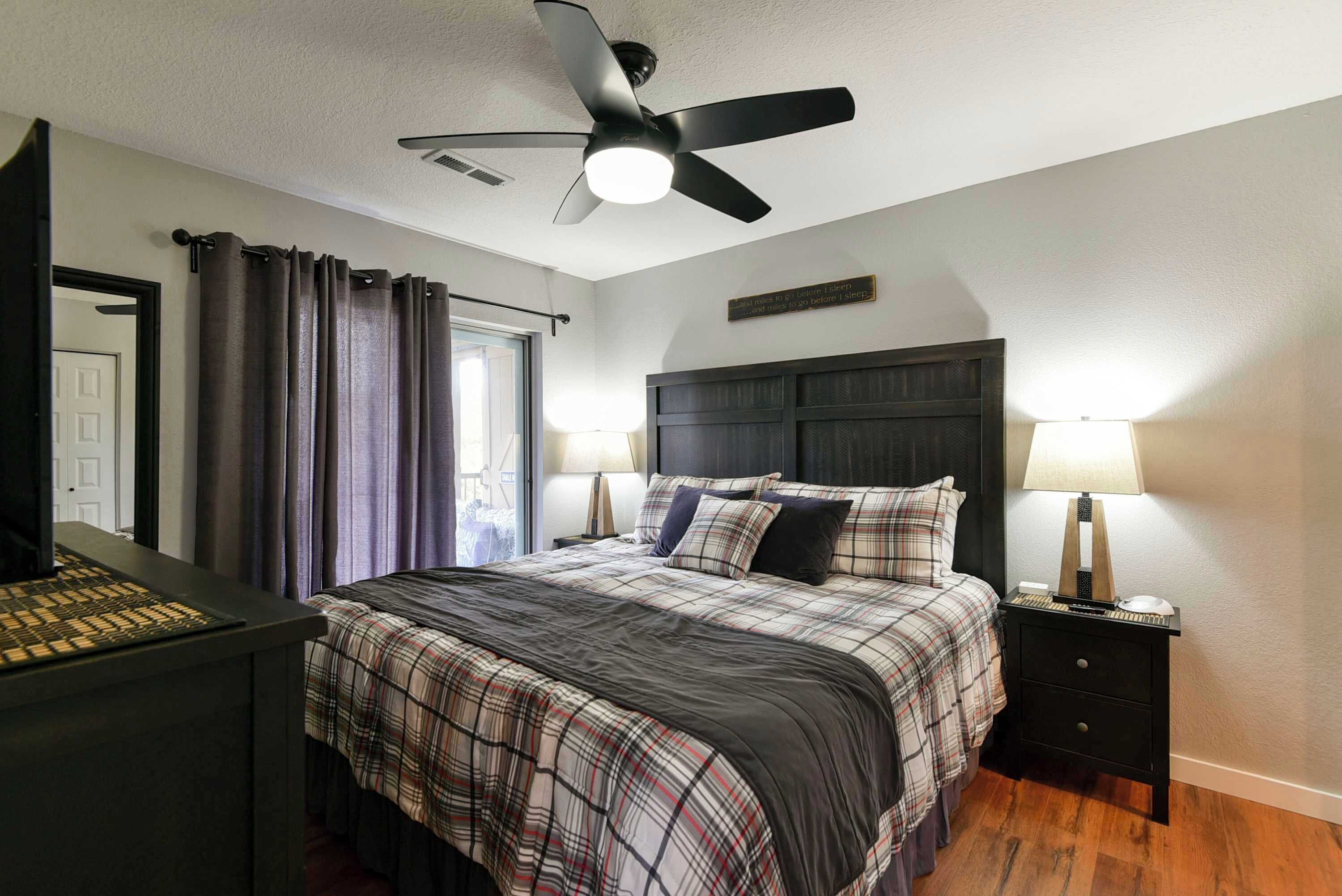 A bedroom with a bed, nightstands, a ceiling fan, and a door.