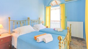 A room with two beds, a window with yellow curtains, an air conditioning unit, and a radiator. - House On The Rocks in Nisaki (Corfu)