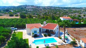 Eine Villa mit Schwimmbad, umgeben von üppiger Vegetation und einer hügeligen Landschaft.
