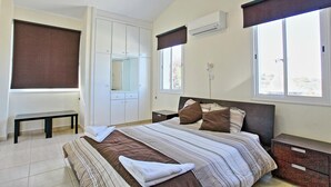 Ein Schlafzimmer mit einem Bett, einem Kleiderschrank, einer Bank und einem Fenster mit Vorhängen.
