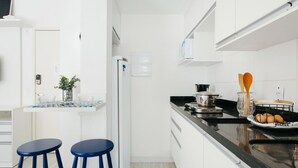 Eine moderne Küche mit weißen Schränken, einer schwarzen Arbeitsplatte, zwei blauen Barhocker und einem kleinen Topf mit Pflanze auf der Arbeitsfläche.