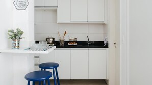 Eine kleine Küche mit weißen Schränken, einer schwarzen Arbeitsplatte und einem blauen Hocker.