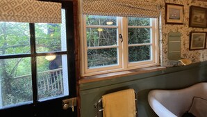 A bathroom with a bathtub, a window with a patterned curtain, and a wooden ceiling.