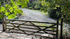 A gravel path leading through a wooden gate into a garden with various plants and trees.