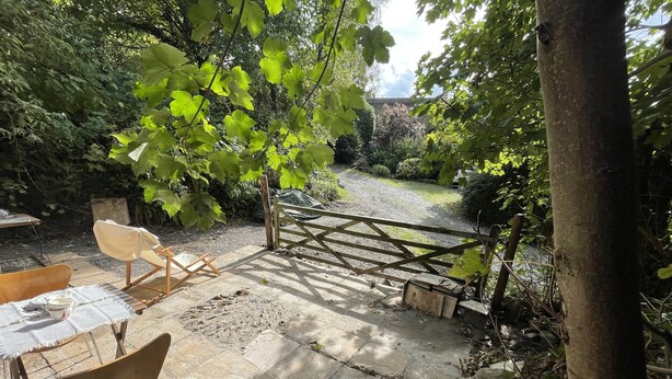 A patio area with a table and chairs, a wooden gate, and a gravel path leading to a garden.