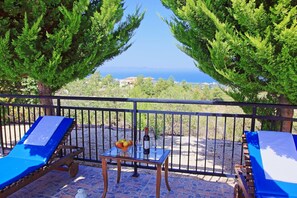 A terrace with two blue lounge chairs, a table with a wine bottle and glasses, and a view of the sea. - Marilena Sunset Villa Dio (Ayia Marina Chrysochous)