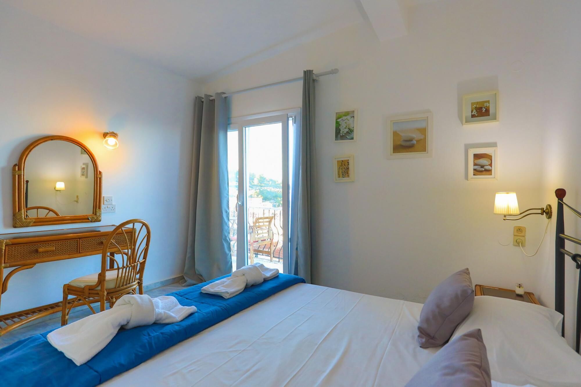 A hotel room with a bed, a wooden chair, a desk with a mirror, and a view of the outdoors through a window.
