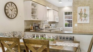 A modern kitchen with a built-in microwave, a clock, and a dining area with a wooden table and chairs. - Valley View Treehouse - Holiday Hills Branson Golf Resort Outdoor Pools (Branson)