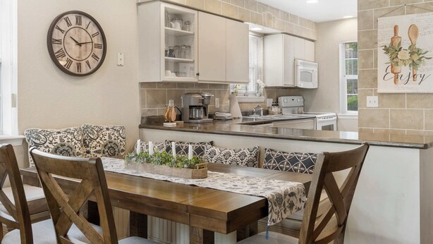 A modern kitchen with a wooden dining table, patterned cushions, and a clock on the wall. - Valley View Treehouse - Holiday Hills Branson Golf Resort Outdoor Pools (Branson)