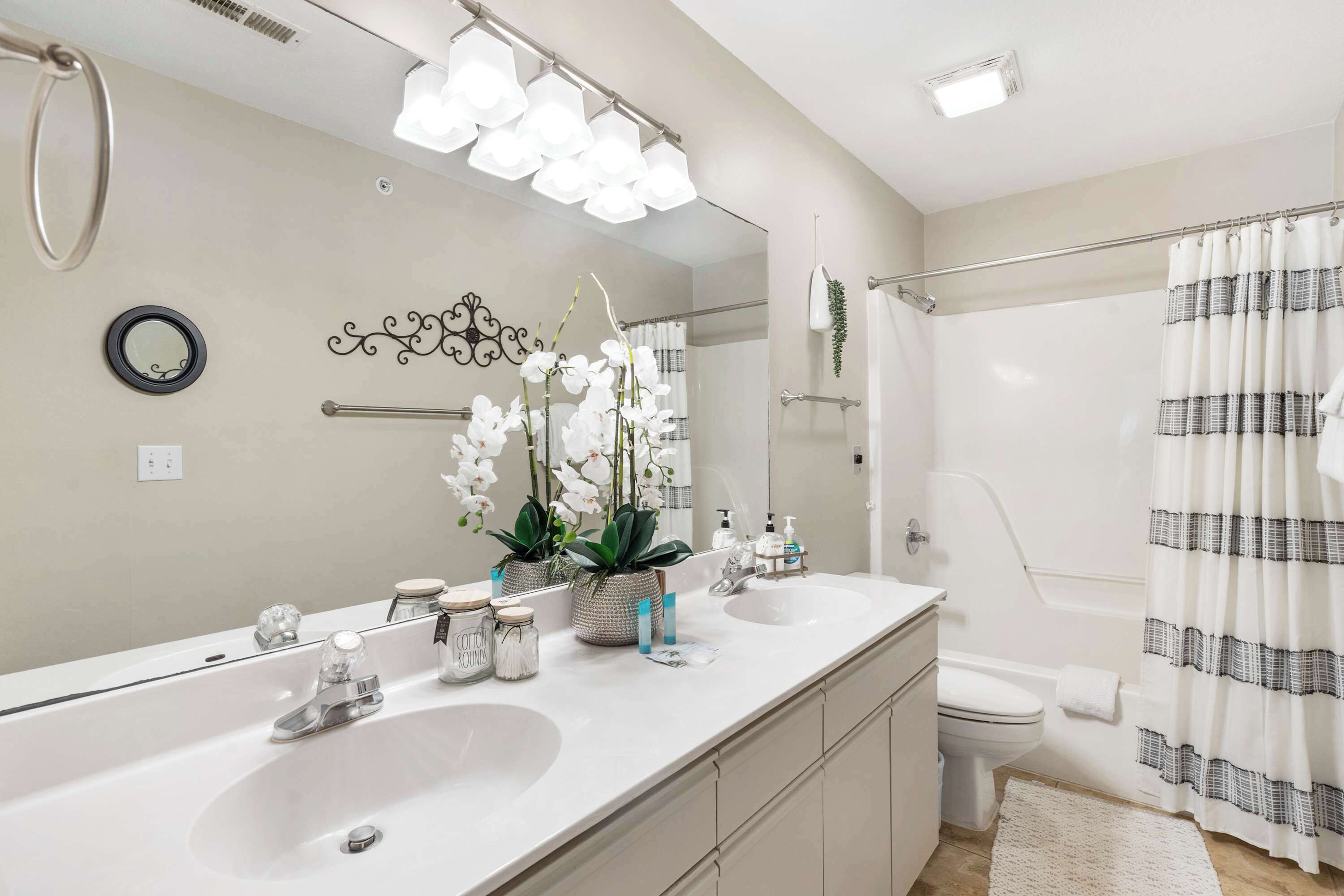 A modern bathroom with a large mirror, two sinks, a toilet, and a shower area.
