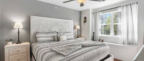 A bedroom with a bed, nightstands, a ceiling fan, and a window with curtains.