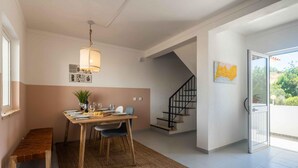 A dining area with a wooden table, chairs, and a hanging light fixture. There is a staircase leading to an upper floor and a door to the outside. - Casa Almar by Portucasa (Lagoa)