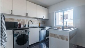 A modern kitchen with stainless steel appliances, a built-in oven, and a window providing natural light. - Casa Almar by Portucasa (Lagoa)