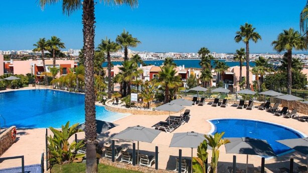 A resort with a large pool, palm trees, and a view of the city. - Casa Almar by Portucasa (Lagoa)