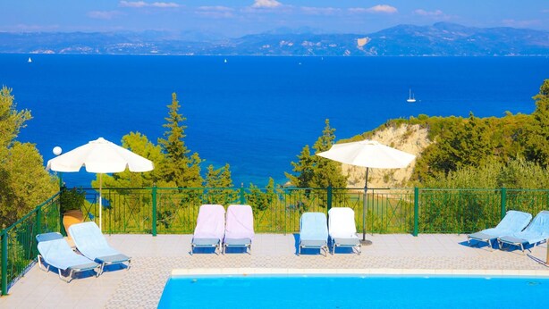 A poolside area with lounge chairs and umbrellas, overlooking a large body of water and distant mountains. - Antigoni Villa Dio in Longos (Paxos)