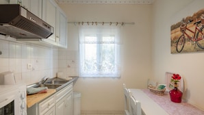 A small kitchen with white cabinets, a stove, a sink, and a window with a curtain. - Antigoni Villa Dio in Longos (Paxos)