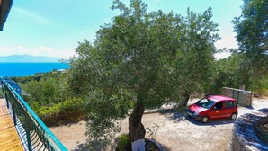 A red car parked near a tree in a garden with a view of the sea. - Antigoni Villa Dio in Longos (Paxos)