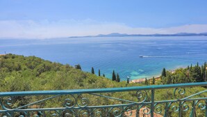 A coastal view with a clear sky, a boat on the water, and a green landscape with trees. - Villa Ariadni in Nisaki (Corfu)