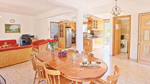 Amplia sala de estar con una mesa de comedor de madera, sofás rojos y una cocina con armarios de madera y lavadora incorporada.