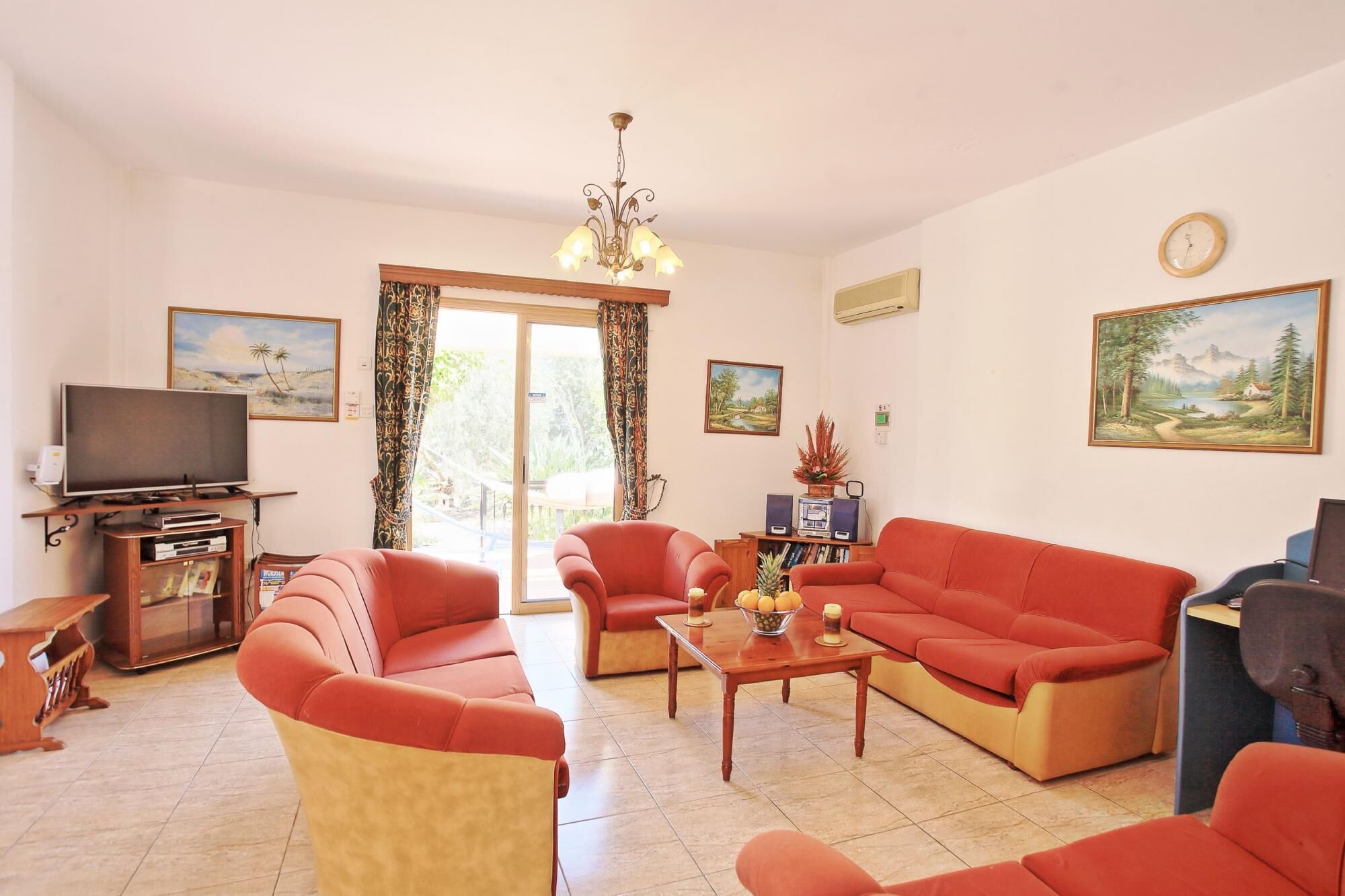 Ein Wohnzimmer mit Fernseher, roten Sofas, einem Couchtisch und einer Deckenleuchte.