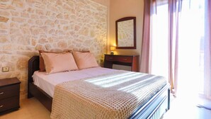 Ein Schlafzimmer mit Steinwand, einem Bett mit gemustertem Überwurf, einem Nachttisch, einer Kommode, einem Spiegel und einem Fenster mit Vorhängen.