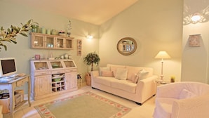 A cozy living room with a white sofa, a small white armchair, a wooden cabinet with glass doors, a green rug, and a mirror on the wall. - Prasini Luxury Cottage (Paxos)