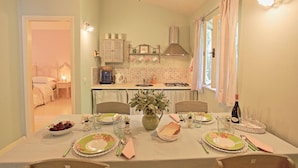 A dining area with a table set for four, a kitchen in the background, and a bedroom visible through an open door. - Prasini Luxury Cottage (Paxos)